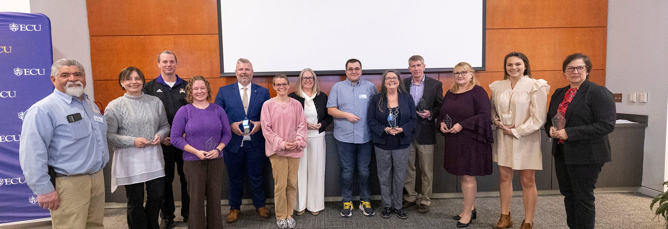 Group of award-winning people stand together in front of projection screen