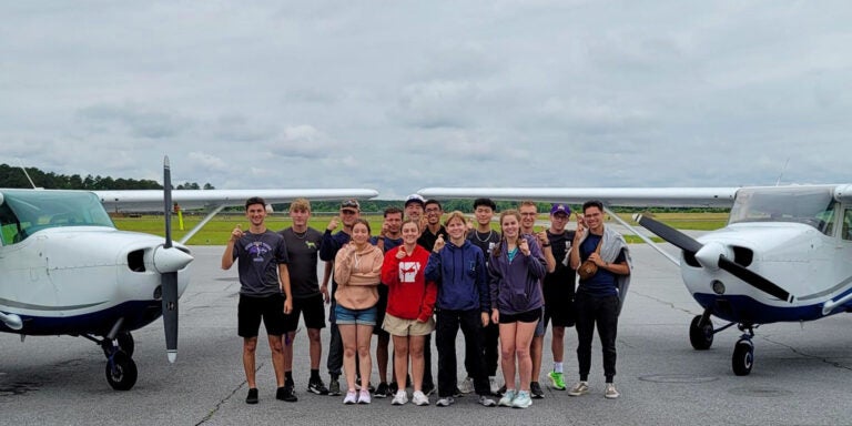 High-schoolers stand in a group between two planes.