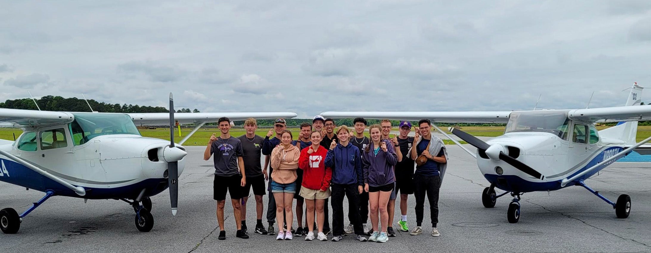 High-schoolers stand in a group between two planes.