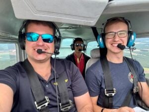 Three males sitting inside an airplane with headshots on their ears.