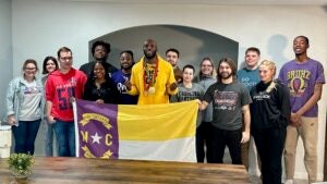 A group hold up a purple and gold NC flag.