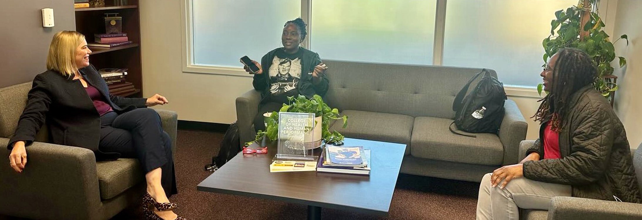 Three women talking and lounging in office setting.