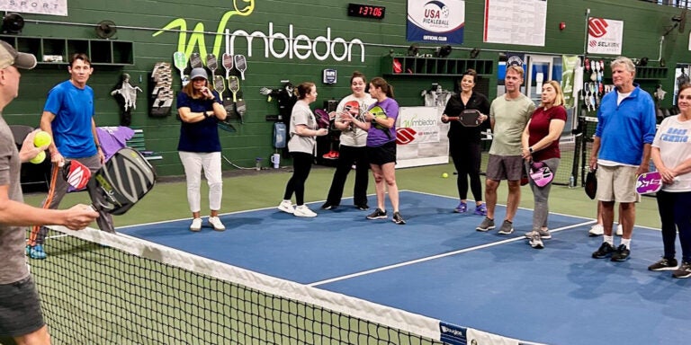 People standing and listening to instruction on pickleball court.