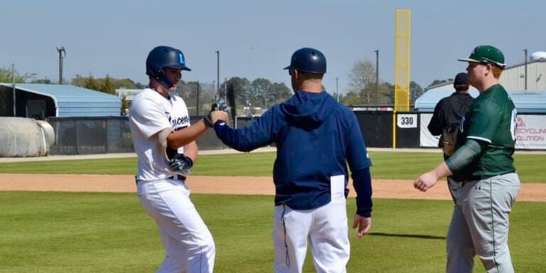 A baseball coach first-bumps his college player near first base.