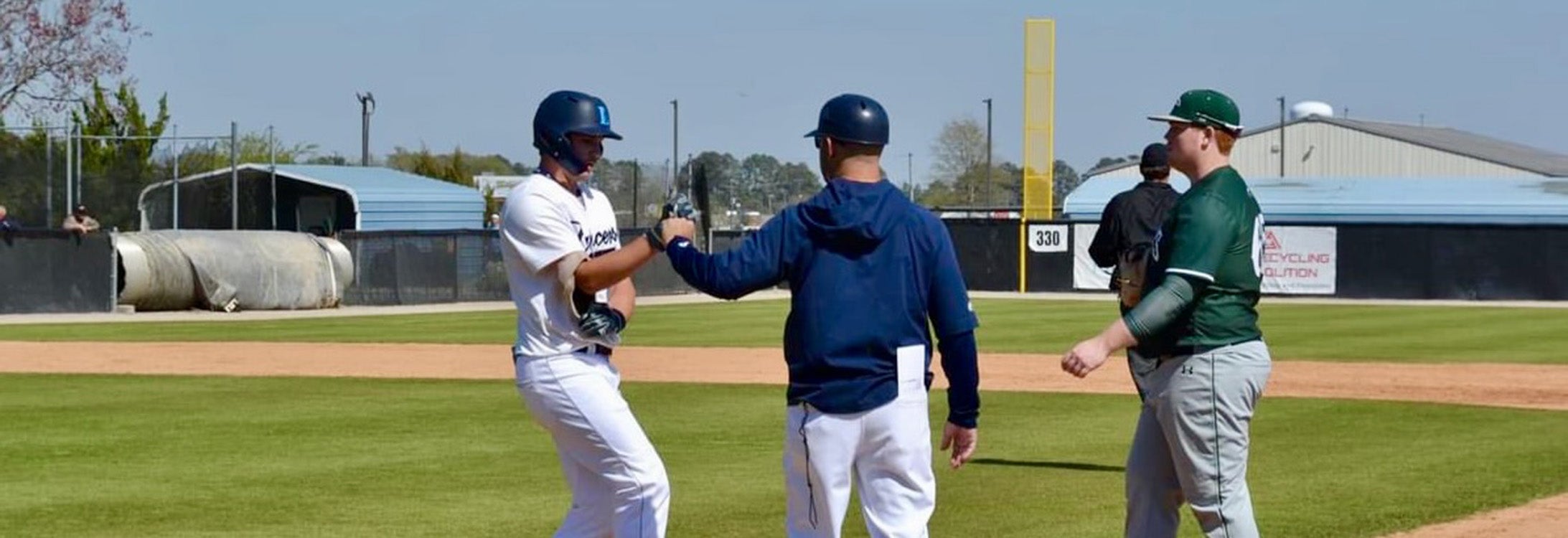 A baseball coach first-bumps his college player near first base.