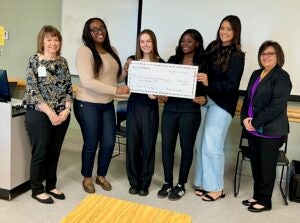 Students stand with mock big check in classroom.