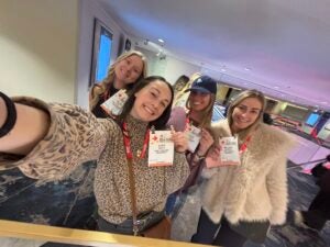 Four girls take a selfie together holding their lanyards. 