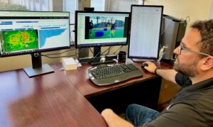 A professor looks at computer screens, showing soccer images and data, at his desk.